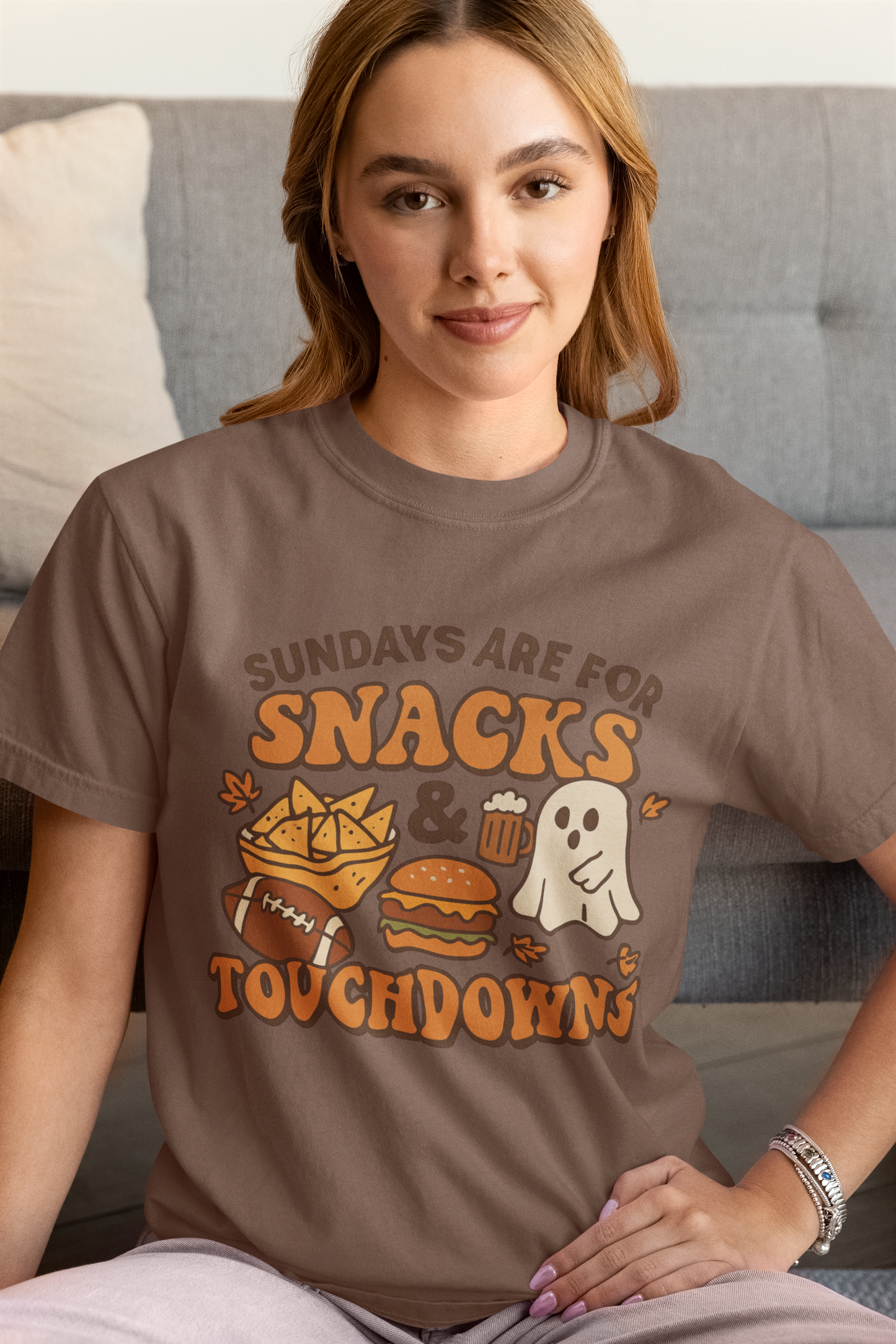 Woman wearing a brown t-shirt with a graphic design sitting on a couch.