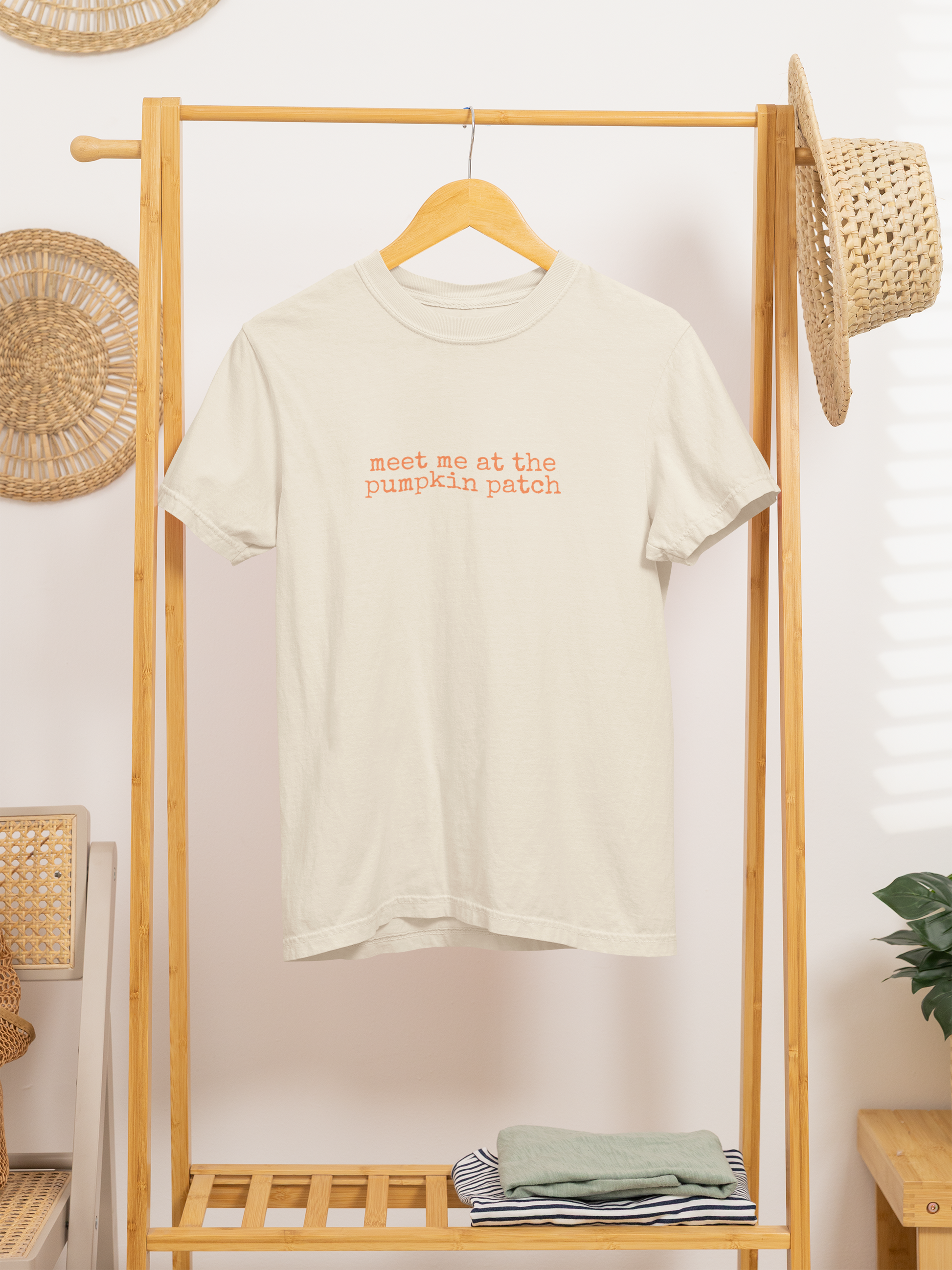 Beige t-shirt with 'meet me at the pumpkin patch' text on a wooden rack.
