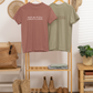 Two t-shirts on a rack with boots and decor items in a room.