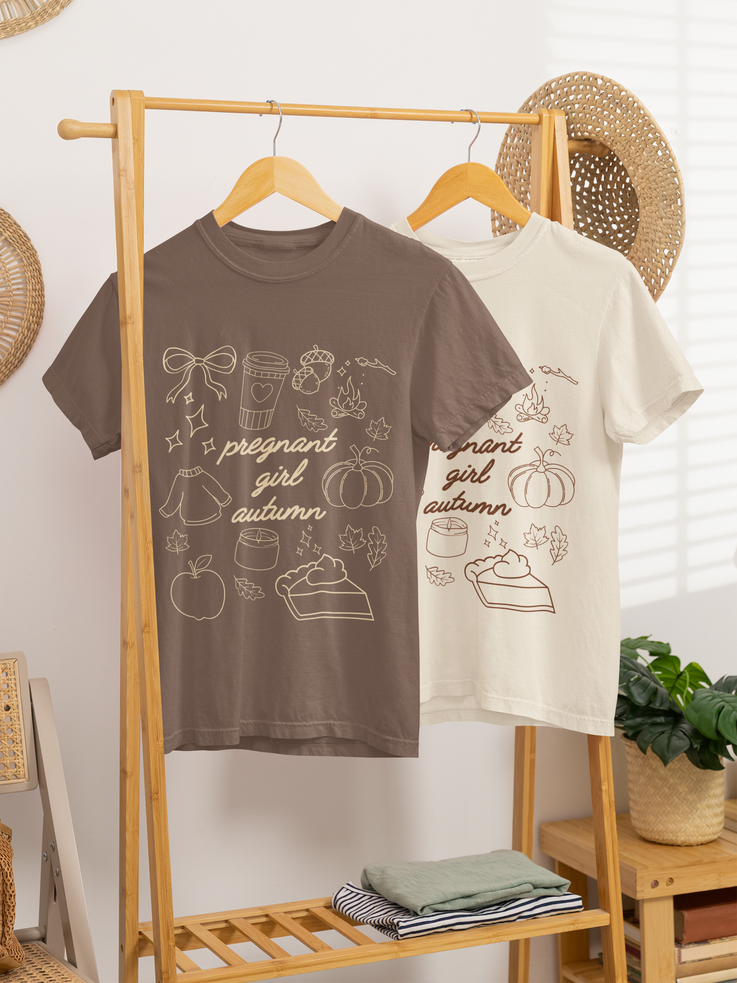 Two t-shirts with autumn-themed designs hanging on a wooden rack.