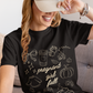 Woman wearing a black t-shirt with 'pregnant girl fall' design and a beige cap.