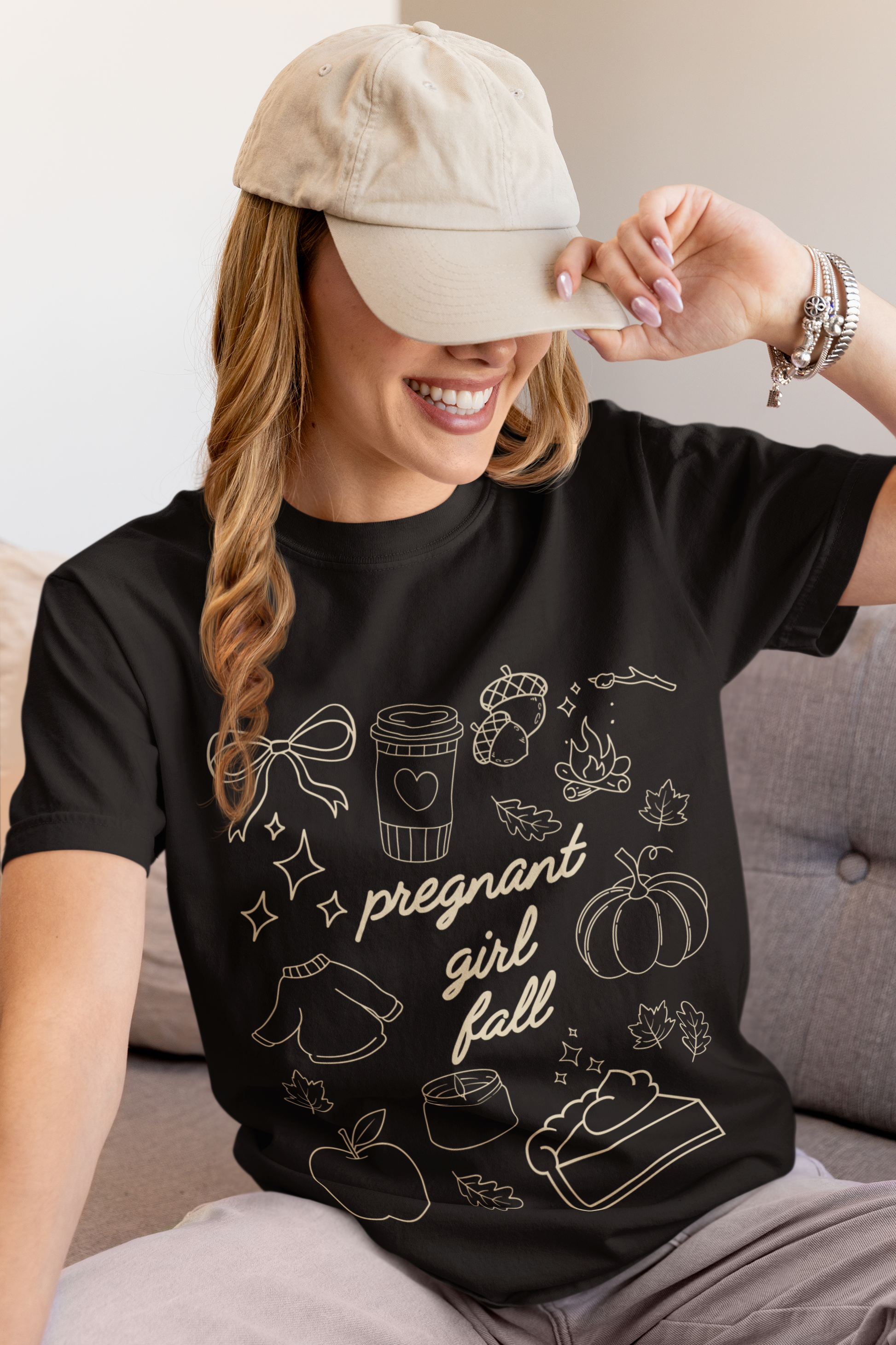 Woman wearing a black t-shirt with 'pregnant girl fall' design and a beige cap.