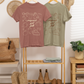 Two t-shirts on a rack with boots and a plant in the background