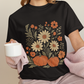 Person wearing a black t-shirt with floral and pumpkin design, holding a white mug.
