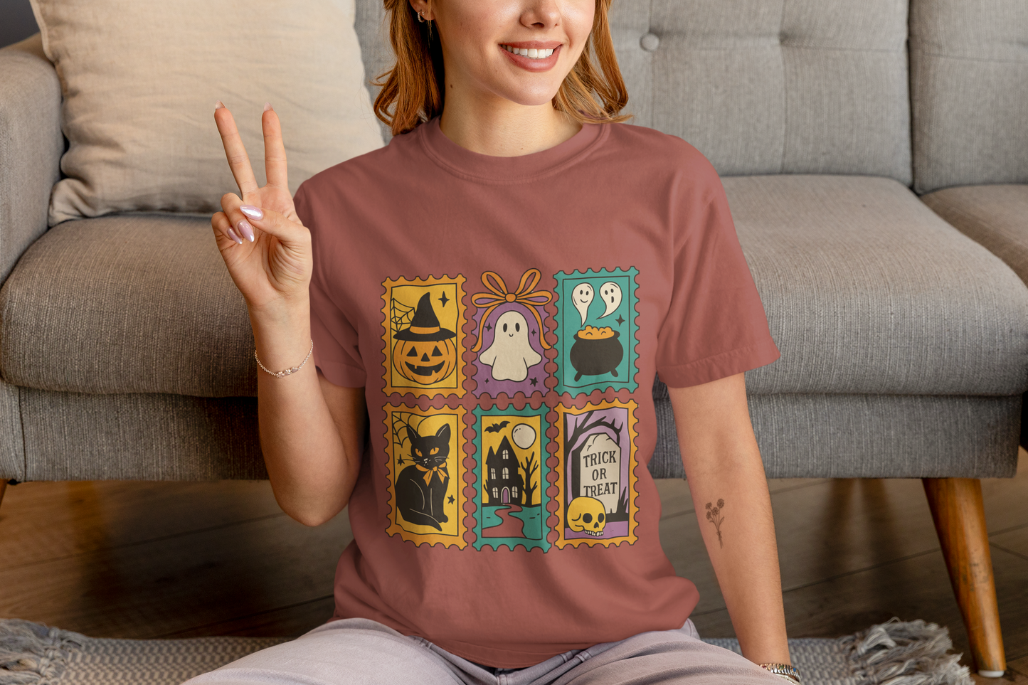 Person wearing a brown t-shirt with Halloween-themed designs, sitting on a couch.
