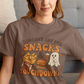 Woman wearing a brown t-shirt with a graphic design sitting on a couch.
